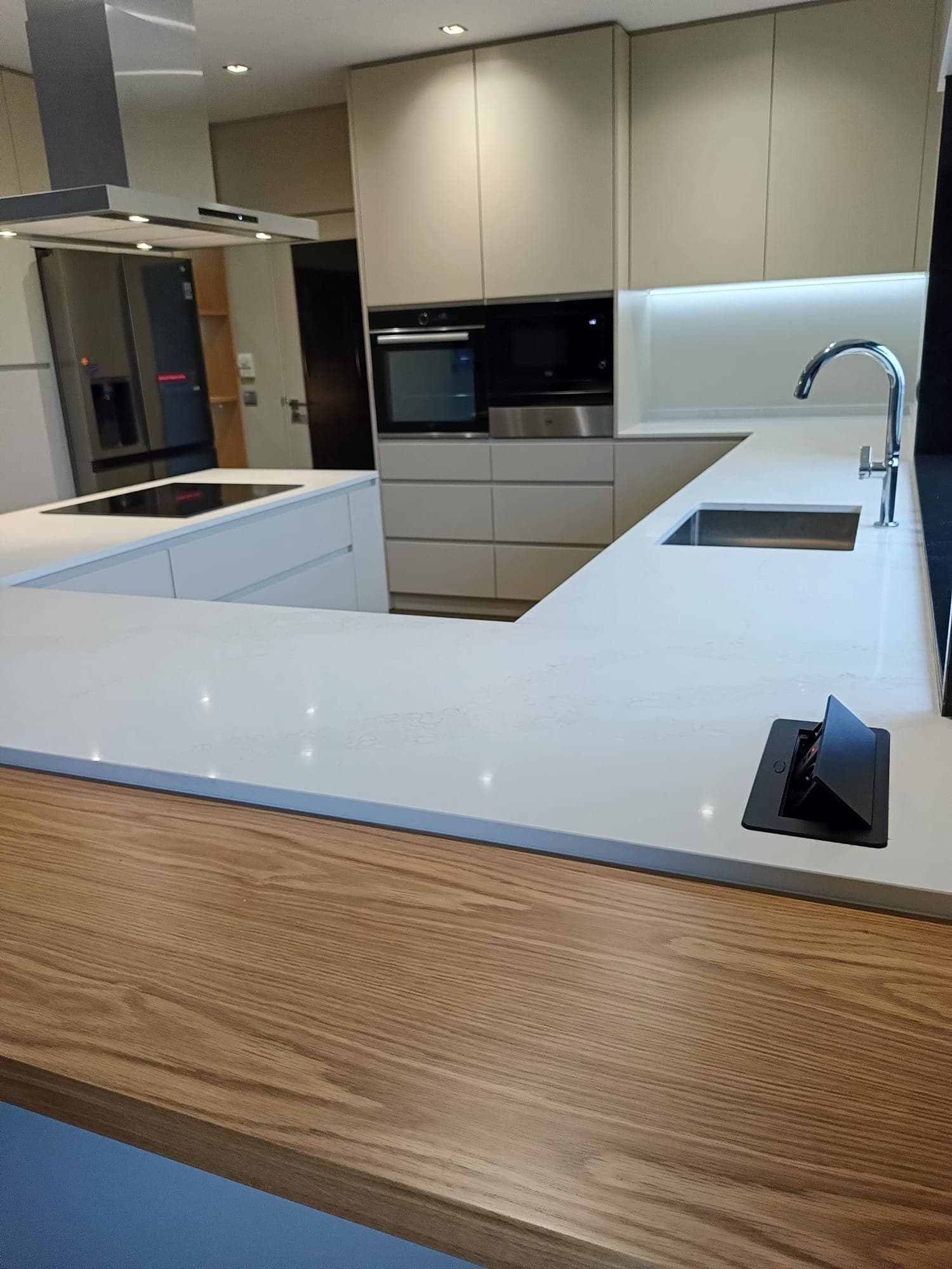 Pormenor de cozinha com bancada em quartzo, cascata em madeira e tomada retrátil