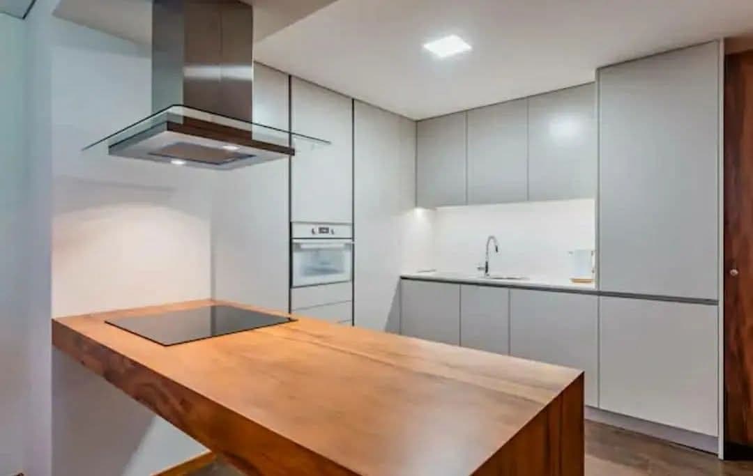 Cozinha minimalista em lacado claro com exaustor de ilha e tampo em madeira